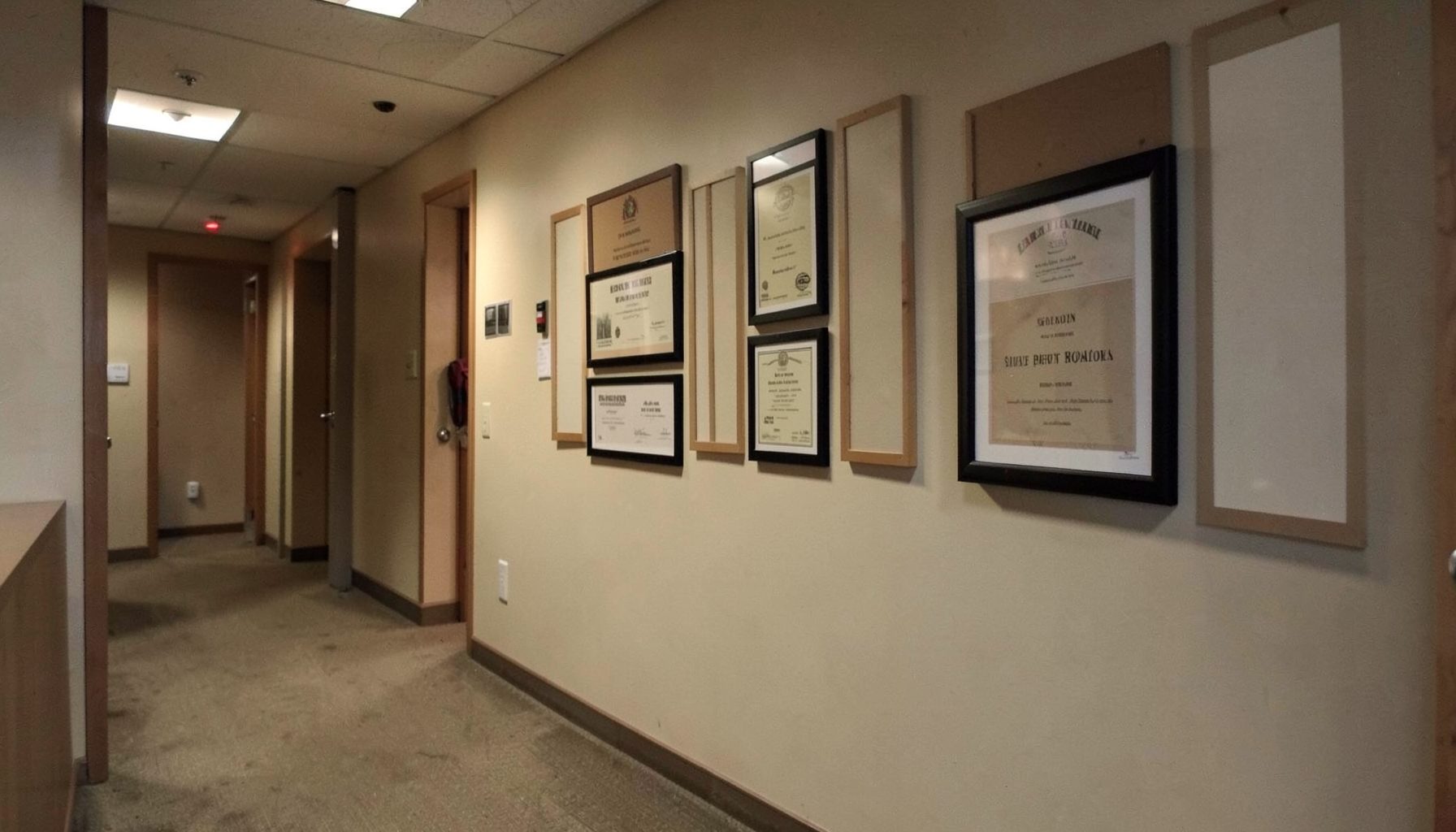 Calm, understated law office hallway with framed credentials on the wall and warm ambient lighting, evoking trust and professionalism