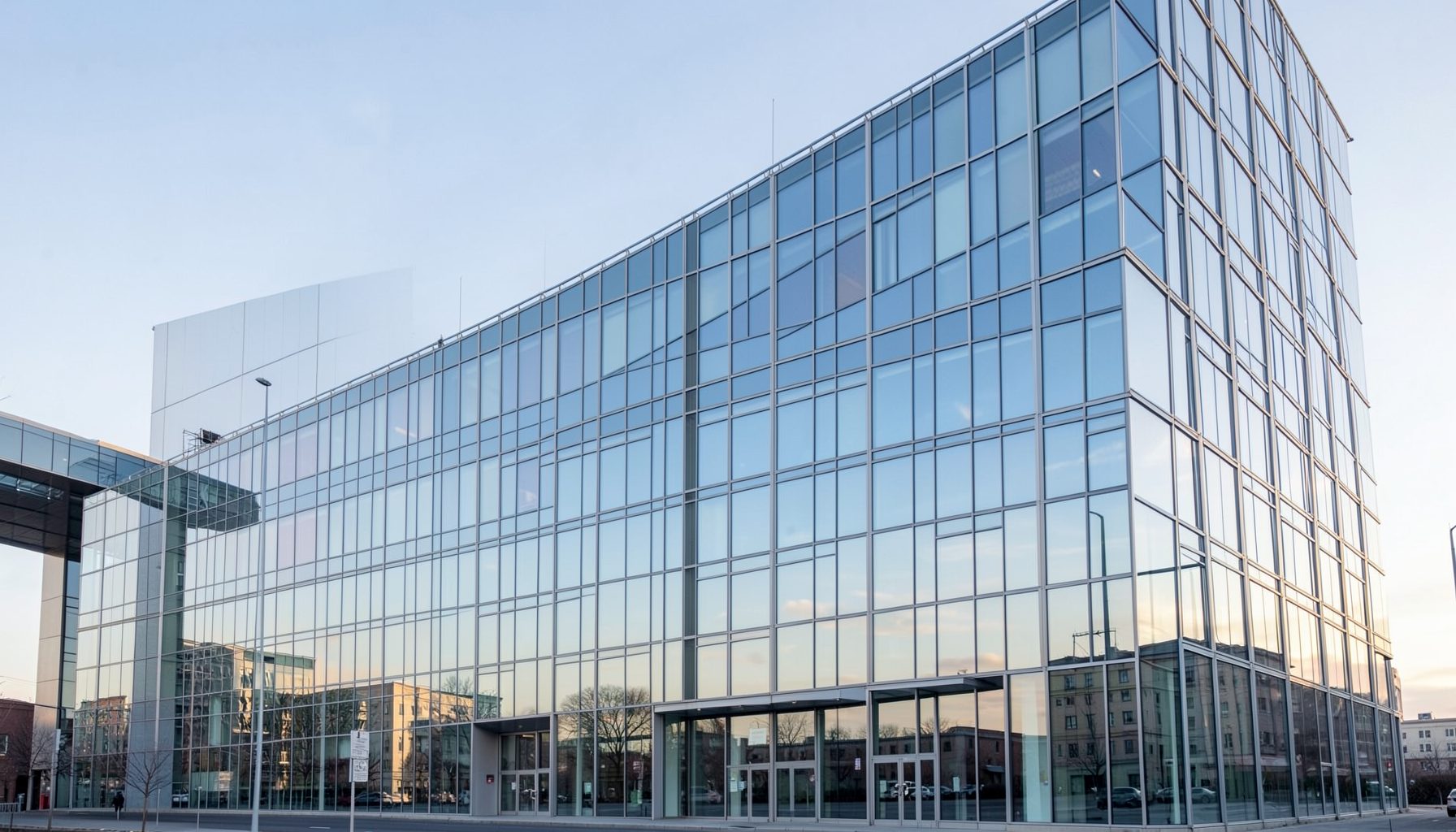 Wide-angle view of a modern glass office building facade under soft morning light, predominantly steel blue and pale gray